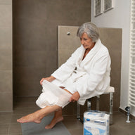 Woman in a bathrobe sitting on a toilet with a box of tissues next to her.