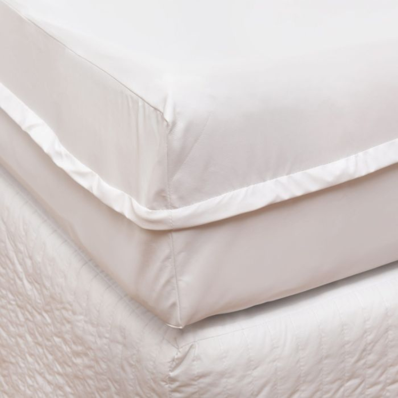 Close-up of a beige quilted coverlet on a bed with a white pillow.