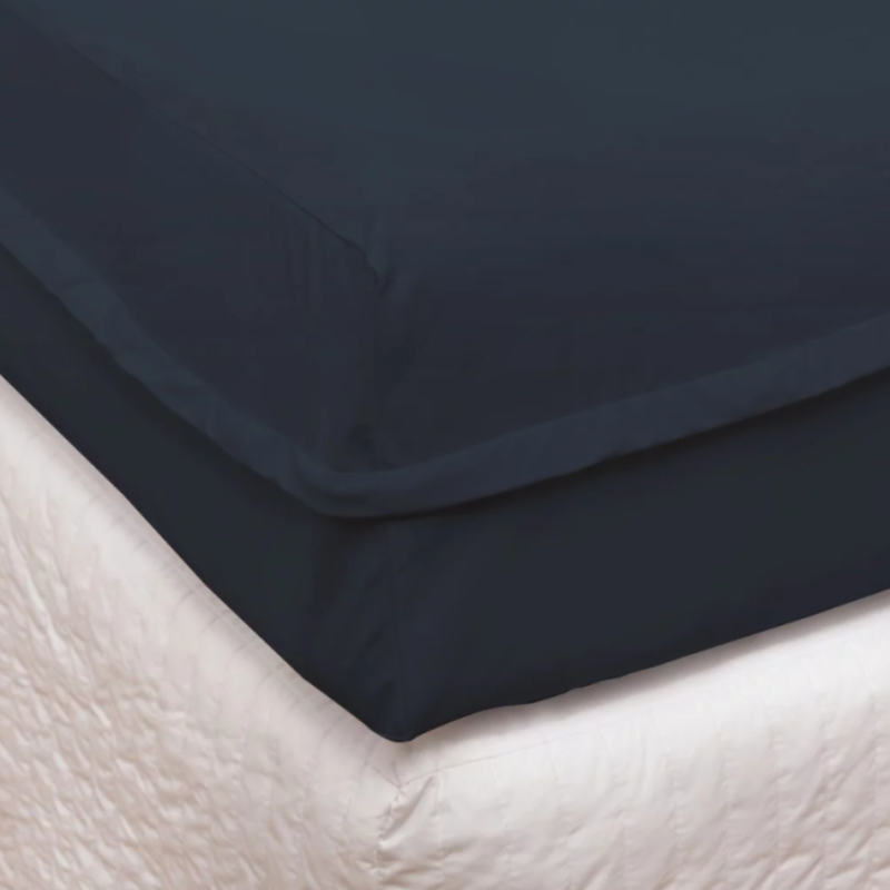 Dark blue fitted sheet on a bed with a light-colored mattress cover.