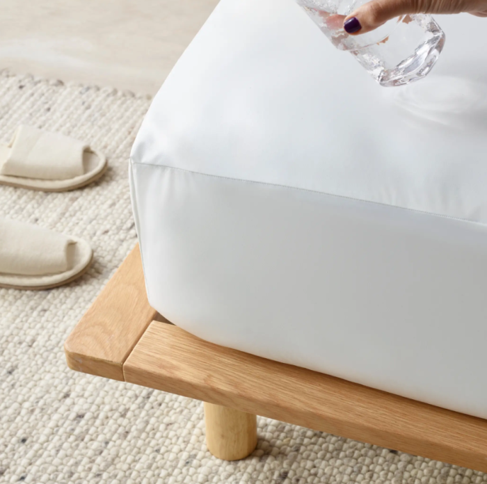 White mattress on a wooden platform with a hand holding a glass of water.