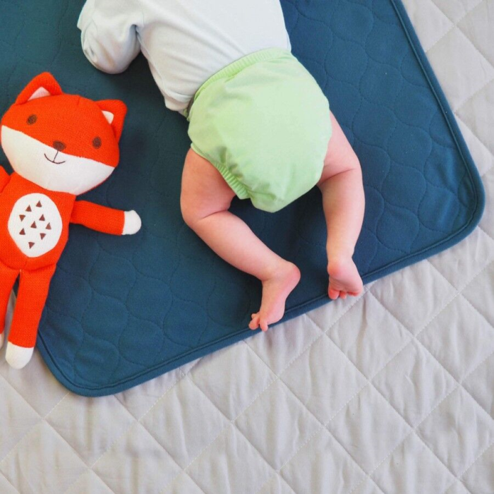 Baby in green diaper with a red fox plush toy on a blue mat