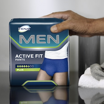 TENA Men Active Fit Pants packaging held by a hand on a reflective surface.