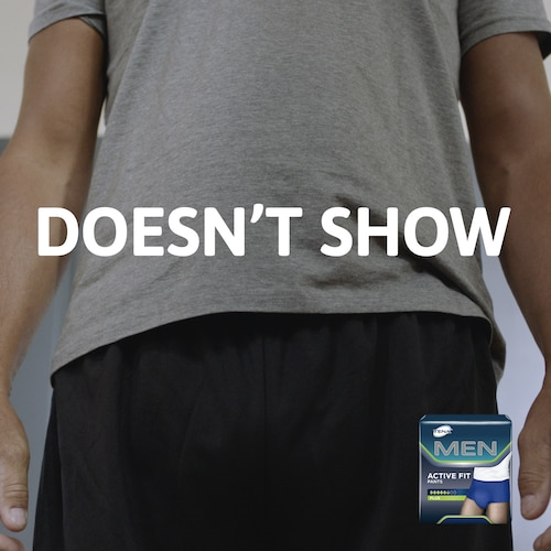 Person wearing a gray t-shirt with a visible stain, text 'DOESN'T SHOW', and a Men's deodorant stick in the corner.