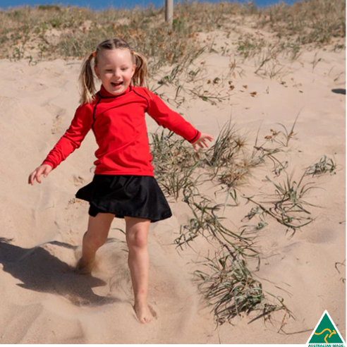 Child in a red shirt and black skirt running on sand dunes