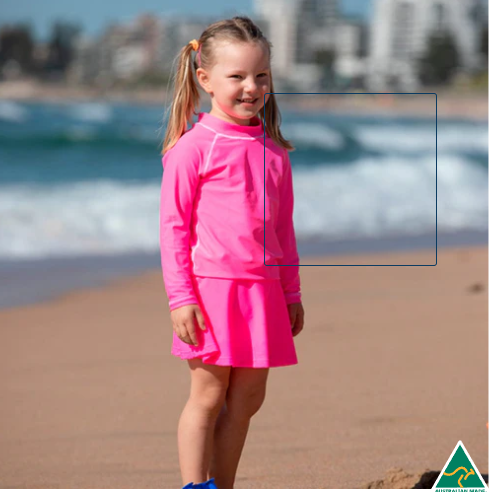 Young girl in a pink outfit standing on a beach with ocean waves in the background