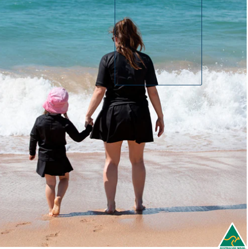 Woman and child walking on a beach with waves crashing behind them